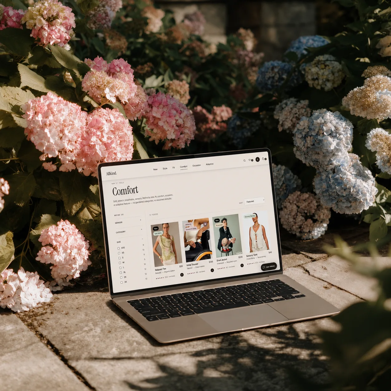 A laptop showing the Allkind browse page, resting among blue and pink hydrangeas.