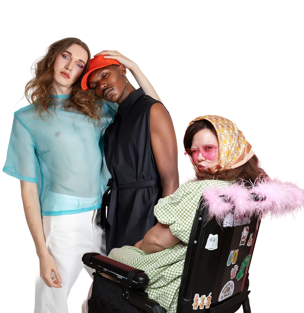Three people in expressive, colourful outfits, one seated in a wheelchair, posing together against a white background.