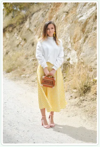 Persona photo for Amanda, standing on a sunny path in a yellow skirt and white sweater.