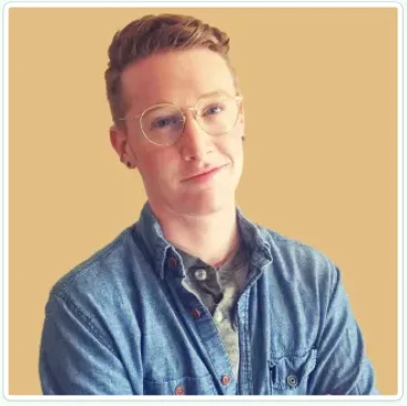 Persona photo for Riley, in glasses and a denim shirt against a yellow wall.